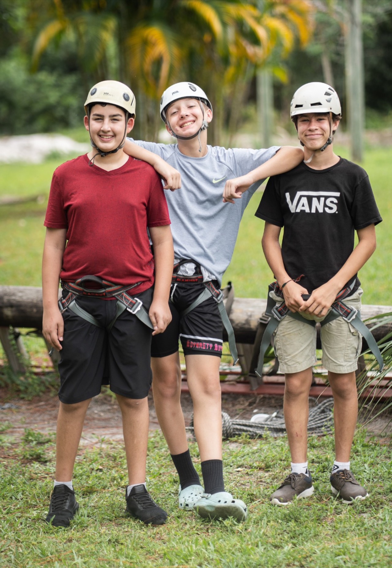 Three campers in helmets and harnesses with arms around each other at the CKids Gan Israel FL ropes course