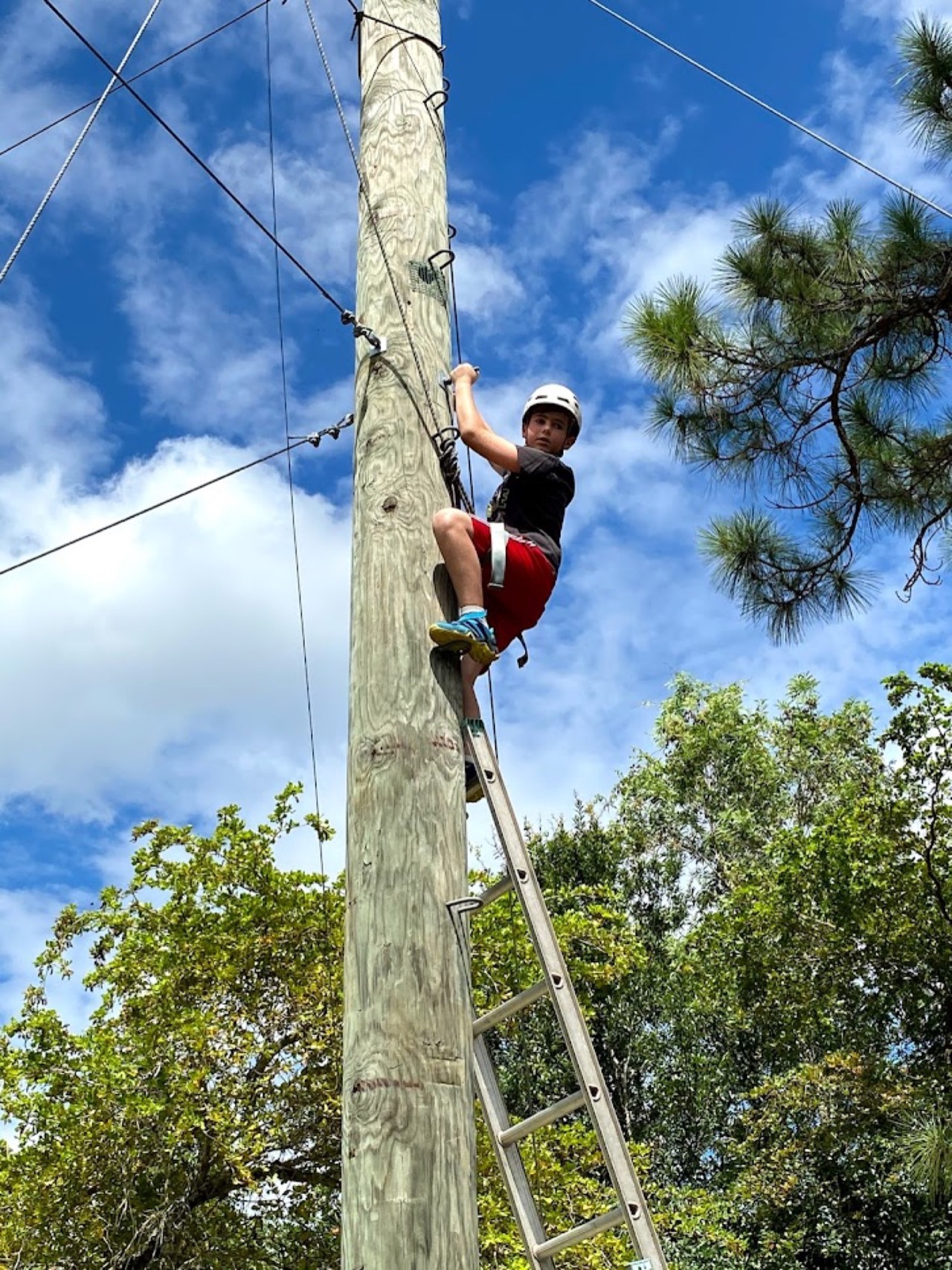 Camper climbing the high ropes course tower against a Florida sky at CKids Gan Israel FL